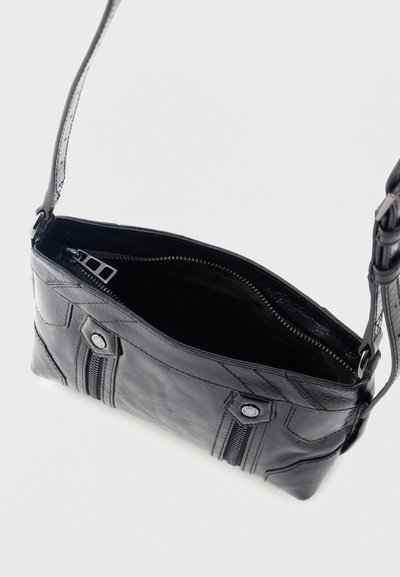 Μαύρη δερμάτινη τσάντα ώμου με εμφανείς ραφές, λεπτομέρειες με φερμουάρ στο μπροστινό μέρος, κουμπιά και ανοιχτό πάνω μέρος που δείχνει το μαύρο εσωτερικό ύφασμα και κλείσιμο με φερμουάρ.