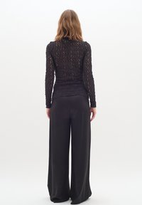 Haut noir en dentelle à manches longues avec une silhouette ajustée, associé à un pantalon noir large et ample, vu de dos.