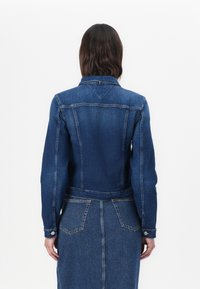Mørkeblå denimjakke med en tett design, knappmansjetter og bakre yoke-detalj; kombinert med et matchende denimskjørt.
