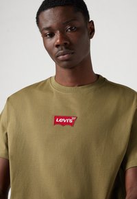 Olive green cotton t-shirt featuring a red embroidered Levi's logo on the chest. Crew neck design with short sleeves and a smooth texture.
