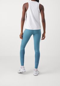Top sin mangas blanco ligero combinado con leggings elásticos color teal que presentan un panel texturizado y un diseño ajustado. Zapatillas deportivas blancas.