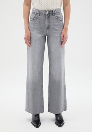 Jean gris taille haute à jambes larges avec ourlet brut, porté avec des bottes noires pointues et un haut sans manches en tricot blanc.