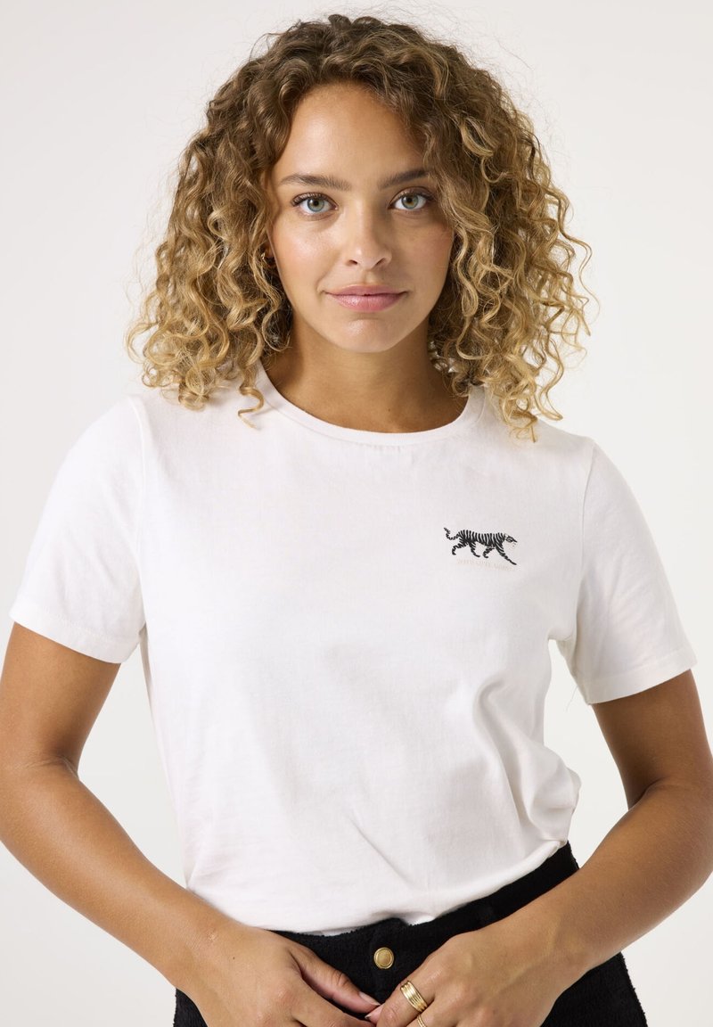 Camiseta de algodón blanca con un pequeño diseño de tigre bordado en negro en el área del pecho izquierdo. Manga corta y cuello redondo.