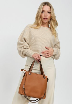 Bruine leren tote bag met dubbele handvatten, gestructureerd ontwerp en decoratieve kettingaccenten aan de zijkanten. Zachte textuur met subtiele nerfdetails.