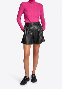 Pull encolure cheminée rose ajusté à côtes associé à un short taille haute en cuir noir. Comprend des poches latérales et une texture lisse. Chaussures noires.