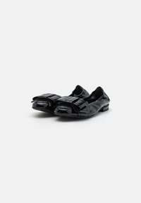 Ballerines noires en cuir verni avec un bout arrondi et un détail en nœud à l'avant. Présentent une texture lisse et brillante, ainsi qu'un petit talon.