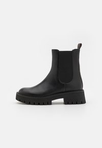 Black leather ankle boot featuring elastic side panels, a chunky tread sole, and a pull tab at the back. Smooth texture with matte finish.