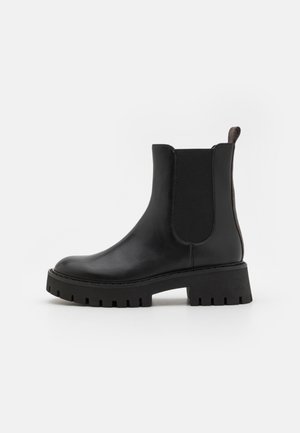 Stivale alla caviglia in pelle nera con pannelli laterali elasticizzati, suola spessa e una linguetta sul retro. Texture liscia con finitura opaca.