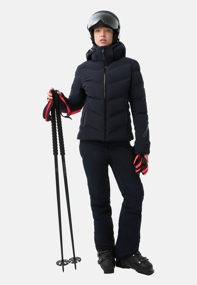 Schwarze Pufferjacke mit hohem Kragen, mit Reißverschlüssen versehenen Taschen und schwarzen Skihosen. Schwarze Skischuhe und -stöcke mit roten Akzenten. Glatte Textur.