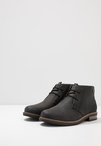 Bottines noires en cuir lisse avec un bout arrondi, un laçage à l'avant et des coutures décoratives le long de la semelle. Talon en bois bas.