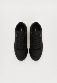 Svarta sneakers med en slät tygöverdel, texturerade detaljer, rund tå och snörning. Har en subtil logotyp på tungan.