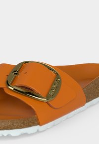 Πορτοκαλί σανδάλι με ευρύ λουράκι, μεγάλη χρυσή αγκράφα, φελλό πάτο και λευκή υφασμάτινη σόλα.