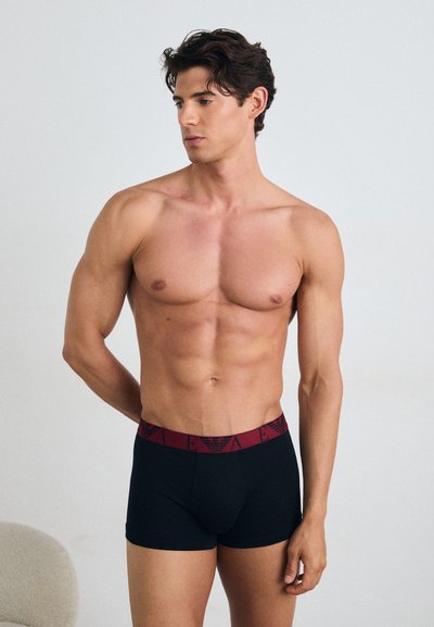 Pantaloni scurți negri tip boxer, cu un tiv elastic vișiniu, având un design cu logo. Modelul are un fizic tonifiat și privește spre lateral.