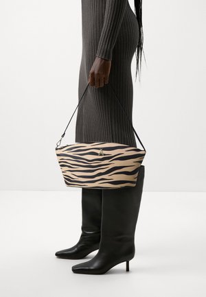 Borsa a strisce tigre beige e nera con forma piatta, chiusura con zip e tracolla nera, tenuta da una persona che indossa un vestito grigio a coste.
