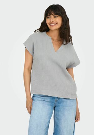 Haut gris clair à manches courtes avec un décolleté en V, fabriqué en tissu texturé. Coupe ample avec un ourlet droit. Associé à un jean bleu clair.