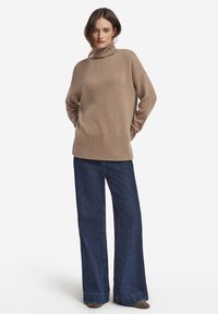 Beige stickad tröja med hög polokrage och ribbad fåll, kombinerad med vida mörkblå jeans. Mjuk textur, avslappnad passform.