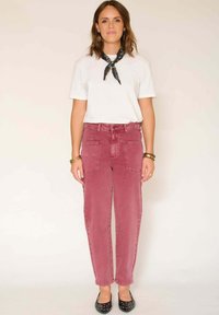 Jean en denim rose délavé avec une taille haute, deux poches avant et une fermeture à bouton, porté avec un t-shirt blanc et des ballerines noires.