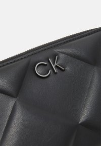 Black puffy leather clutch with quilted texture, featuring raised "CK" logo in silver hardware, and zip closure along the top edge.