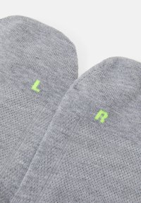 Calzini grigi con texture a coste, caratterizzati da etichette verdi "L" e "R" per il piede sinistro e destro. Il materiale è morbido ed elastico.