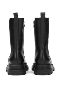 Botas de cuero negro hasta el tobillo con una textura suave, cremalleras traseras y suelas de goma gruesas con profundos surcos, mostrando un diseño moderno.
