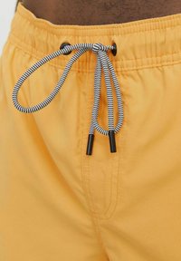 Shorts de bain jaunes avec une taille élastique, dotés d'un cordon noir et blanc et d'un tissu texturé. Comprend deux coutures latérales.