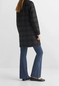 Cappotto a quadri nero e grigio con un design su misura, abbinato a jeans blu a zampa d'elefante e ballerine nere, visto da dietro.