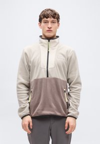 Πουλόβερ από φλις σε μπεζ και καφέ, με εμπρόσθιο φερμουάρ μισού μήκους, τσέπες στα πλάγια με φερμουάρ και όρθιο γιακά. Διαθέτει φερμουάρ με αντίθετο χρώμα για διακοσμητικό αποτέλεσμα.