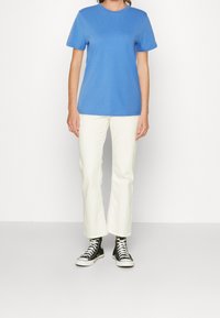 Modrá bavlněná trička s kulatým výstřihem, kombinovaná s bílými rozšířenými džíny a černými vysokými teniskami s bílými tkaničkami.