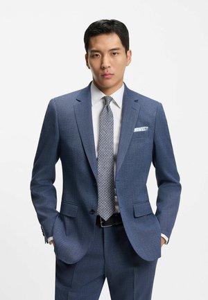 Costume bleu à texture travaillée, associé à une cravate à motifs. Comprend des revers à encoches, un mouchoir de poche et une chemise blanche.