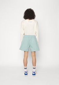 Ljus beige långärmad skjorta med texten "NIGHT ADDICT", tillsammans med mintgröna shorts. Shortsen har ett elastiskt midjeband och en bakficka.