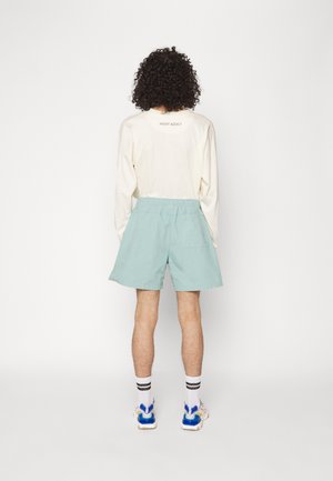 Camisa de manga larga color beige claro con el texto "NIGHT ADDICT", combinada con pantalones cortos verde menta. Los pantalones cortos tienen una cinturilla elástica y un bolsillo trasero.