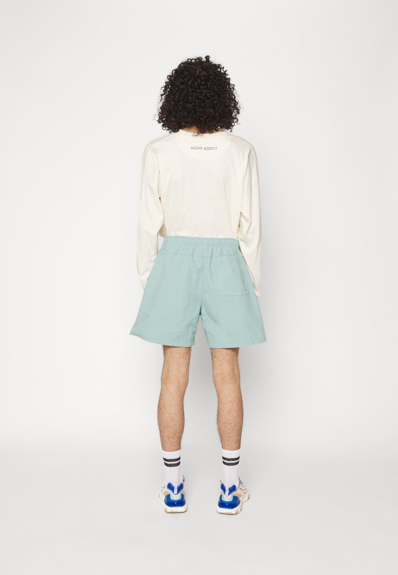 Ljus beige långärmad skjorta med texten "NIGHT ADDICT", tillsammans med mintgröna shorts. Shortsen har ett elastiskt midjeband och en bakficka.