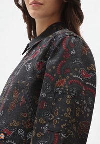 Svart denimjacka med ett paisleymönster i röd, guld och grått. Inkluderar en bröstficka och en design med krage.