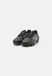 Black soccer cleats with a sleek design, featuring a textured upper, gold accents, and multiple black studs on the sole for traction.