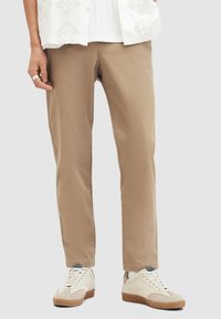Beige puuvillahousut slim fit -mallilla, joissa on sivutaskut, yhdistetty valkoisiin mokkanahkakenkiin ja teksturoituun valkoiseen paitaan.