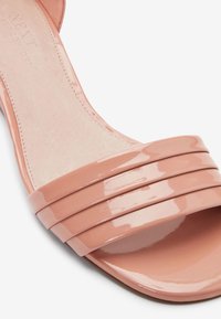 Sandale à glissière en cuir verni rose avec trois bretelles horizontales et une finition lisse et brillante. Semelle intérieure rembourrée avec un intérieur neutre.