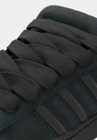 Czarny sneaker z teksturowaną tkaniną i trzema poziomymi paskami. Posiada grube czarne sznurowadła oraz wyściełany kołnierz.