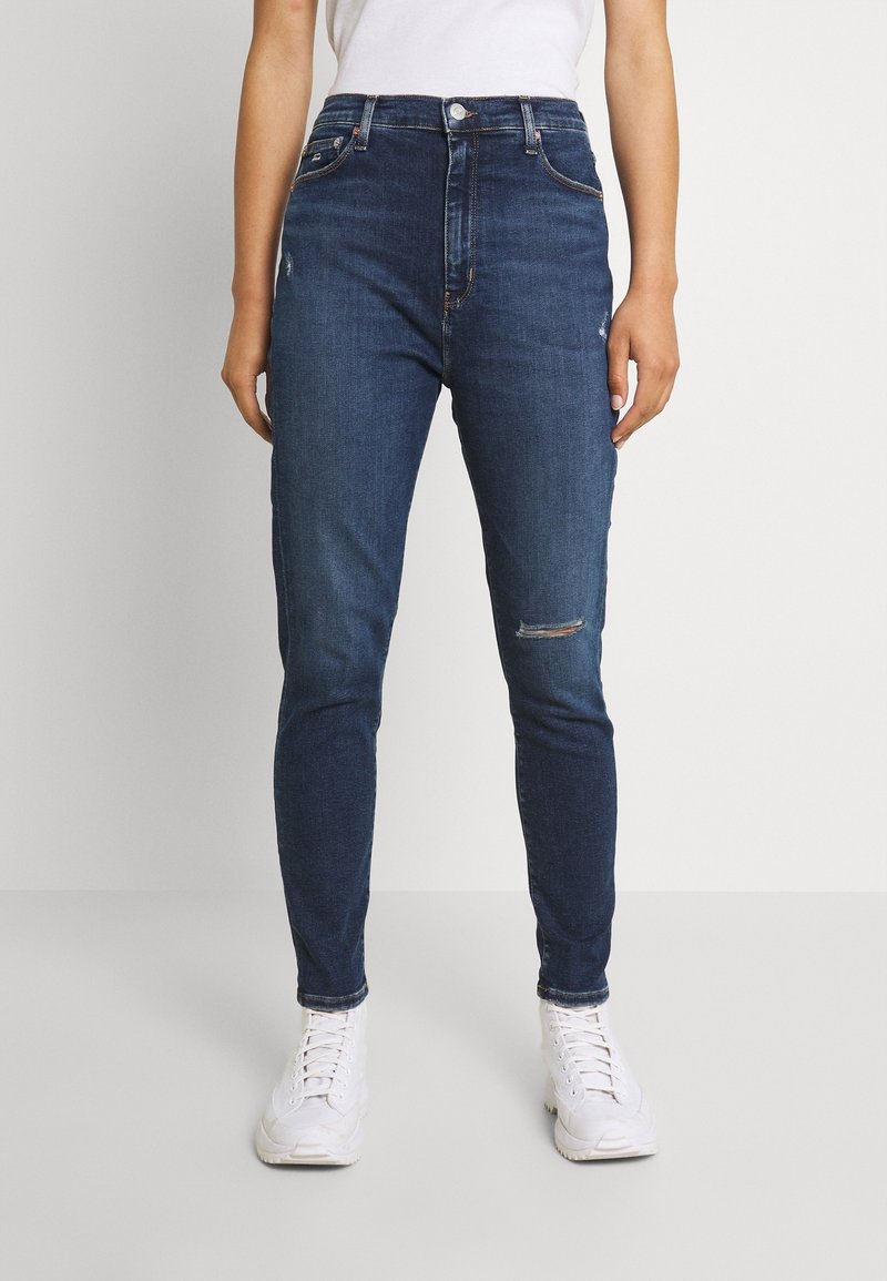Jeans ajustados en denim azul oscuro con una cintura alta, que presentan una rodilla desgastada, detalles de costura sutiles y una textura suave.