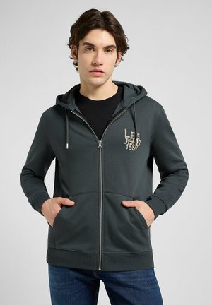 Dark green zip-up hoodie with a drawstring hood, front pockets, and a subtle logo on the left chest, made from soft, textured fabric.