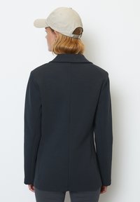 Dark gray jacket with a tailored fit, featuring a notched collar and long sleeves, paired with a light beige cap. Smooth fabric texture.