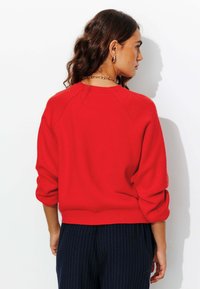 Pull rouge en tissu doux, avec un col rond, des manches raglan et un ourlet légèrement court, associé à un pantalon marine à rayures.