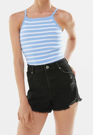 Femme portant un haut sans manches à rayures bleues et blanches et un short en denim noir déchiré taille haute avec des ourlets effilochés.