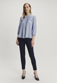 Blusa azzurra chiara con pieghe, scollatura tonda e maniche puff a 3/4, abbinata a pantaloni skinny neri a vita alta e scarpe con tacco nere.