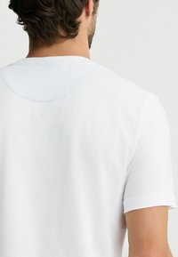 Hvid bomulds t-shirt med rund halsudskæring og korte ærmer. Stoffet er glat med diskrete syninger langs skuldrene.
