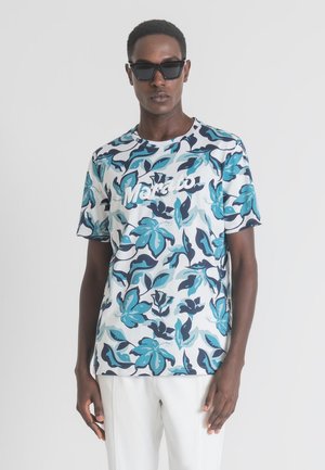 Camiseta de algodón de manga corta con un patrón floral en azul y marino, texto del logo en blanco y cuello redondo, llevada con gafas de sol.