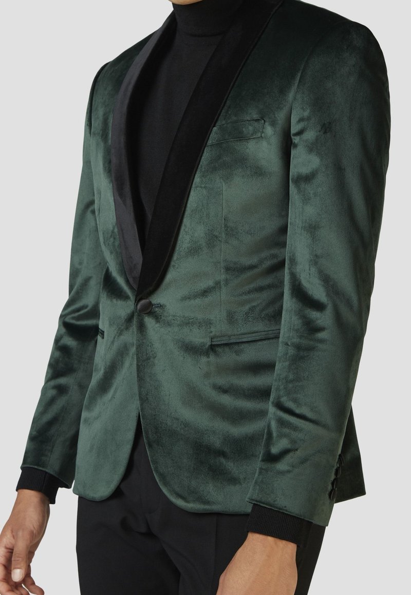 Grüner Samt-Blazer mit schwarzem Satin-Schalkragen, einreihiger Knopfverschluss und schlankem Design. Verfügt über Seitentaschen und strukturiertes Material.