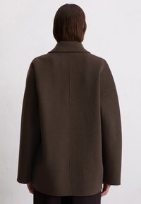 Brauner Wollmantel mit strukturiertem Kragen, übergroßer Passform und gerader Silhouette. Mit einer Mittelnaht hinten und langen Ärmeln.