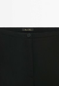 Musta housut, joissa on sileä kangas, tyylikäs muotoilu, nappisuljenta ja merkitty etiketti vyötäröllä. Räätälöity istuvuus ja vähäiset saumat.