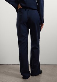 Pantaloni eleganti navy realizzati in tessuto liscio, con frontale piatto, passanti per la cintura e design a gamba dritta. Adatti per abbigliamento formale.