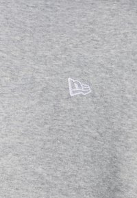 Tessuto di felpa grigio chiaro con una trama morbida, featuring un piccolo logo ricamato bianco nell'angolo in alto a sinistra.